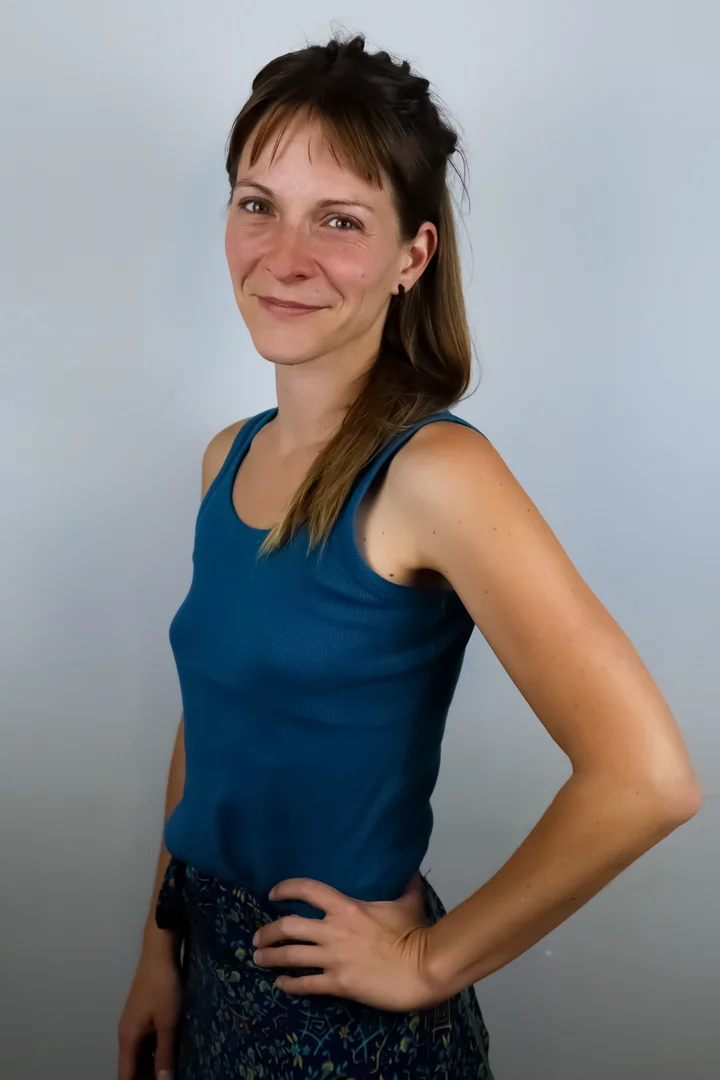 Portret uśmiechniętej młodej kobiety w niebieskiej bokserce stojącej bokiem z ręką na biodrze, na jasnym tle.