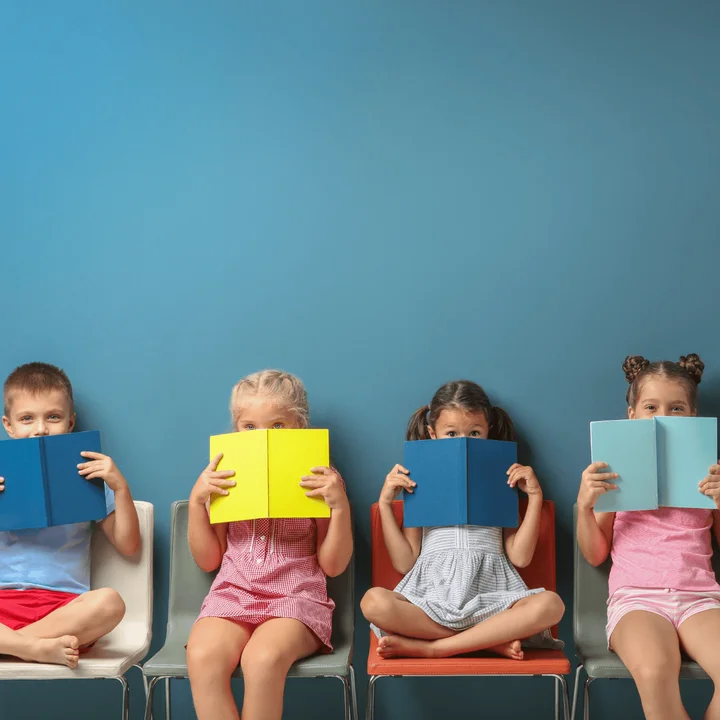 Na zdjęciu widać dzieci, które zasłaniają swoje twarze kolorowymi książkami.