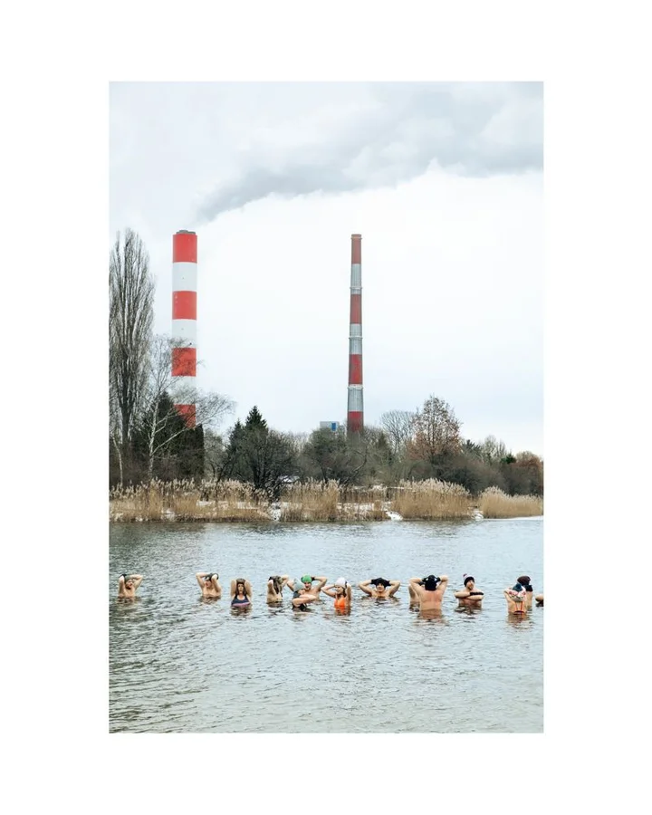 na-pierwszym-planie-ludzie-morsujacy-w-wodzie-za-woda-na-drugim-planie-dwa-dymiace-kominy